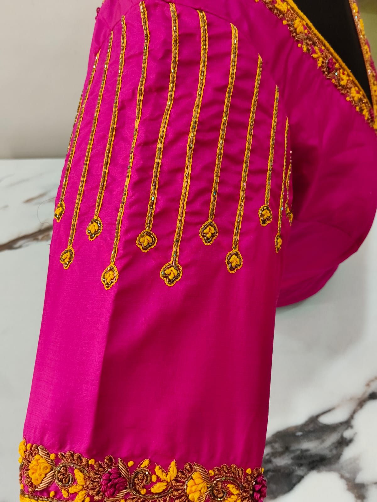 Gold-thread lines ending in small hand-made drops on a fuchsia sleeve